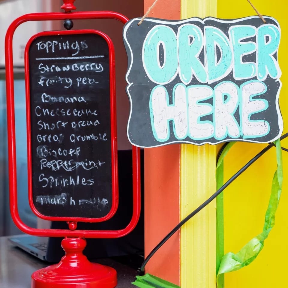 A red chalkboard sign lists dessert toppings next to a black "ORDER HERE" sign.