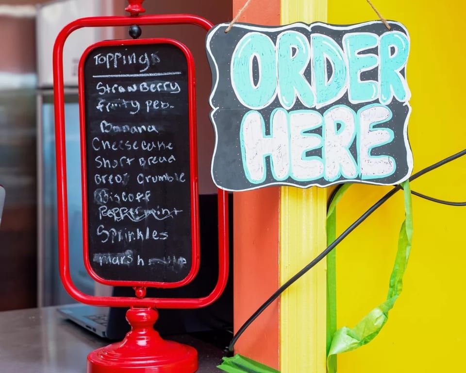 A red chalkboard sign lists dessert toppings next to a black "ORDER HERE" sign.