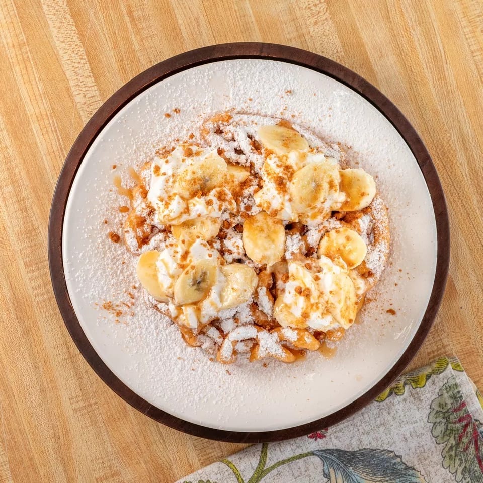 Golden waffle topped with whipped cream, banana slices, caramel drizzle, and powdered sugar.