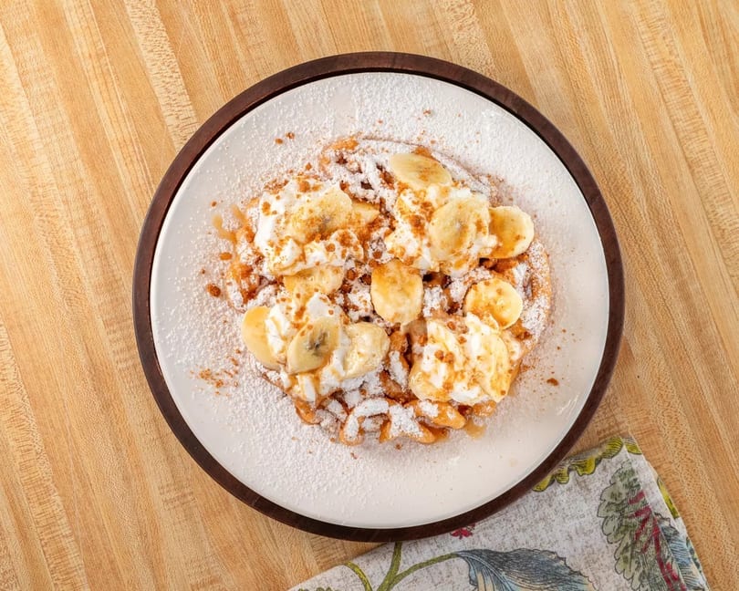 Golden waffle topped with whipped cream, banana slices, caramel drizzle, and powdered sugar.