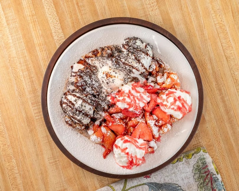 Funnel cake topped with strawberries, whipped cream, chocolate syrup, and powdered sugar.