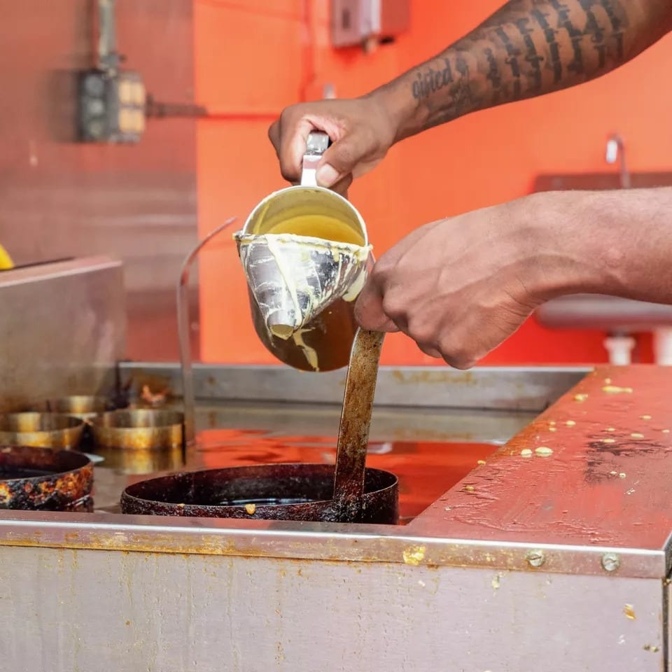 Hands pour batter from a metal pitcher into a deep fryer with circular molds.