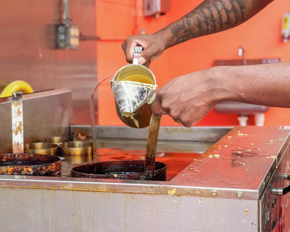 Hands pour batter from a metal pitcher into a deep fryer with circular molds.