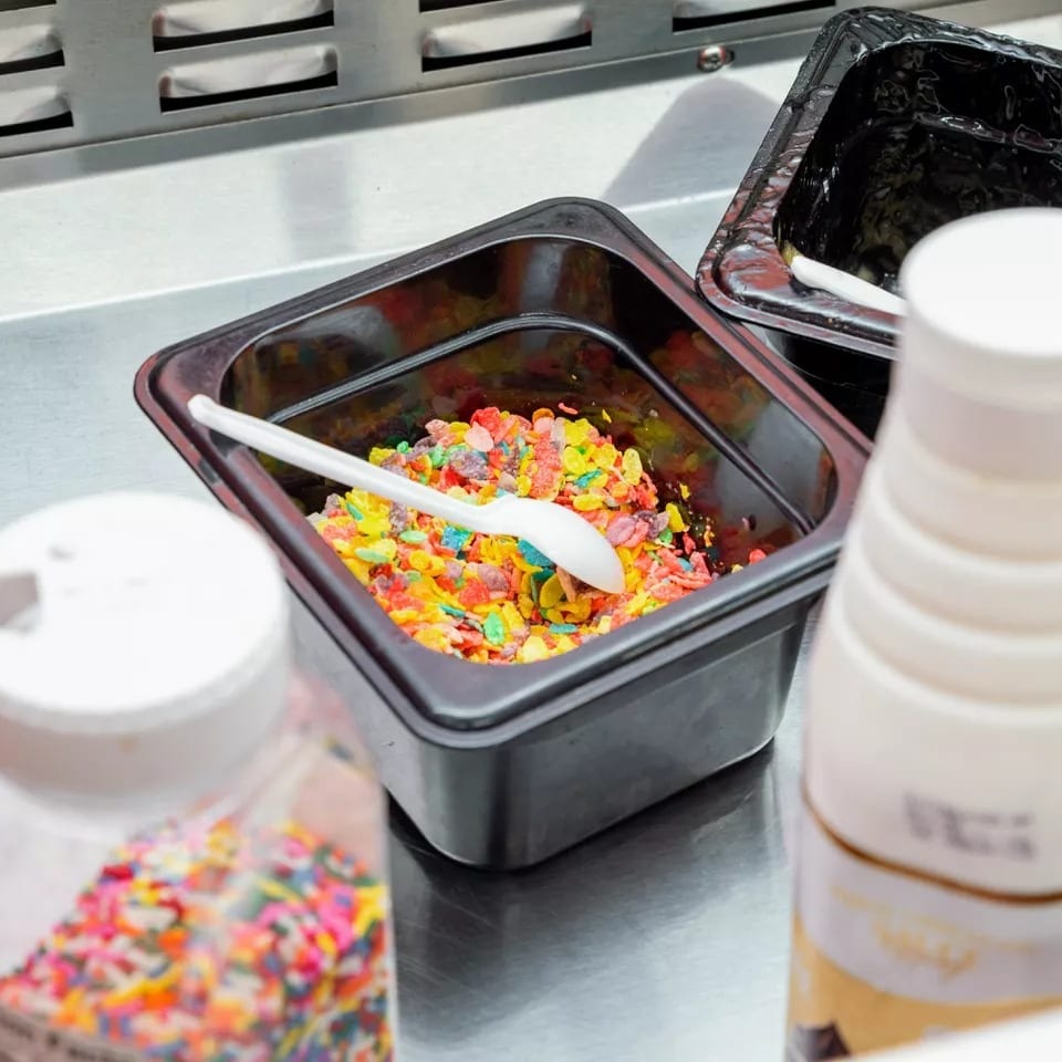 Colorful cereal and sprinkles in containers on a metal counter, ready as dessert toppings.