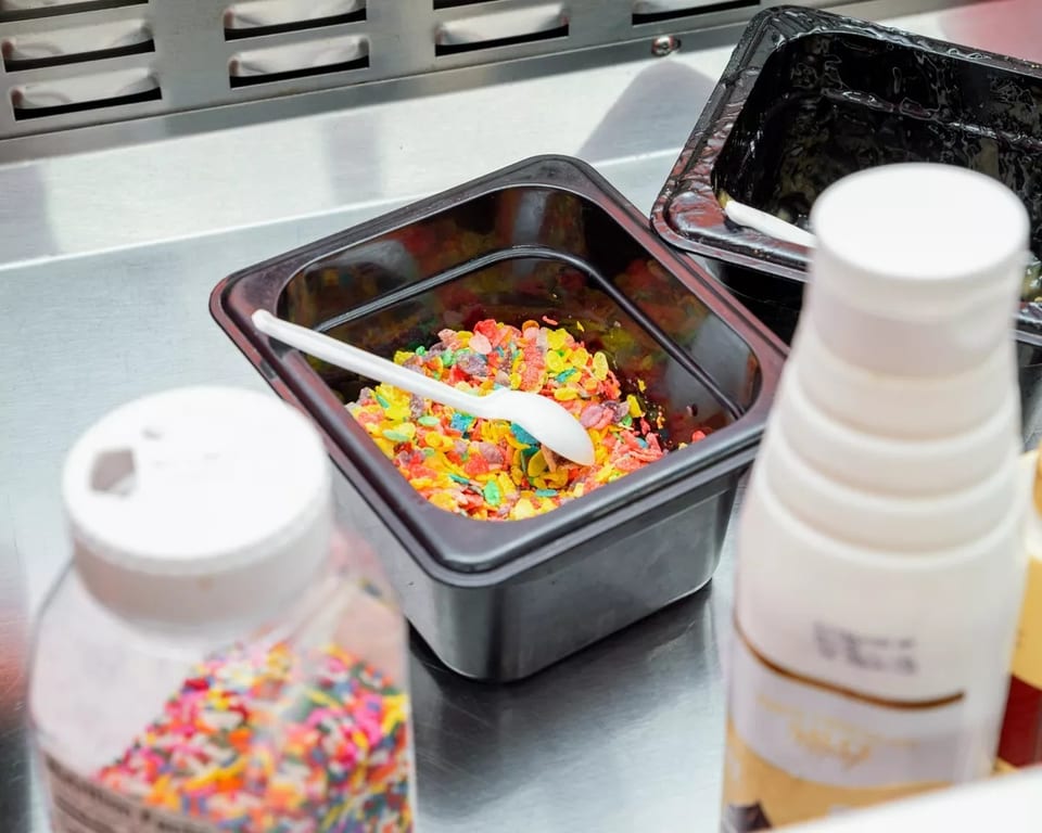 Colorful cereal and sprinkles in containers on a metal counter, ready as dessert toppings.